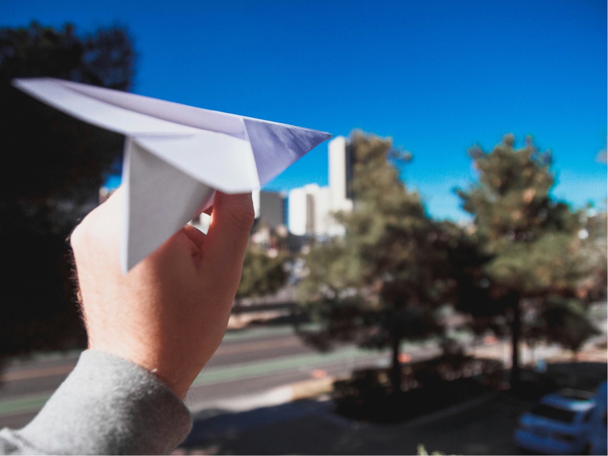 A hand launches a paper airplane into the trees.